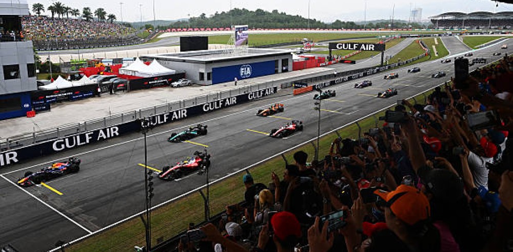 Autos de Fórmula 1 en la recta principal del circuito de Sepang en Malasia con presencia de espectadores en las tribunas.