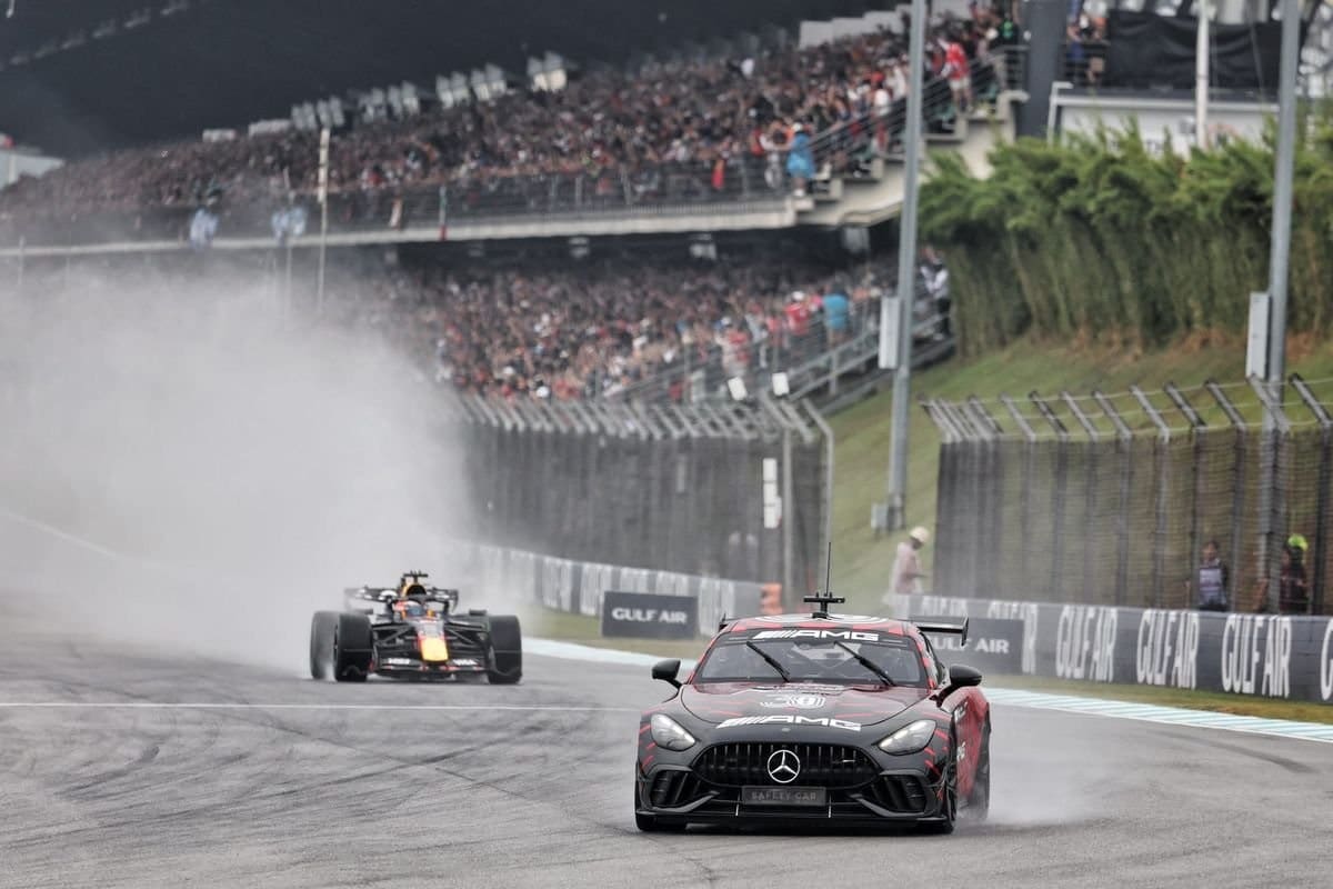 Monoplazas y vehículos de seguridad circulando bajo la lluvia en la pista.